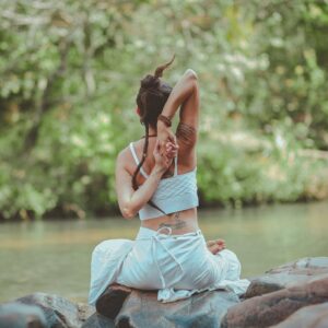 A woman in a yoga pose by a calm river, surrounded by nature, embodying peace and tranquility.