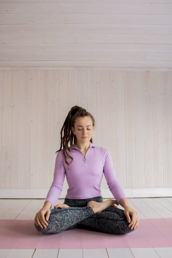 Woman practicing yoga meditation indoors on a pink mat, focusing on relaxation and mindfulness.