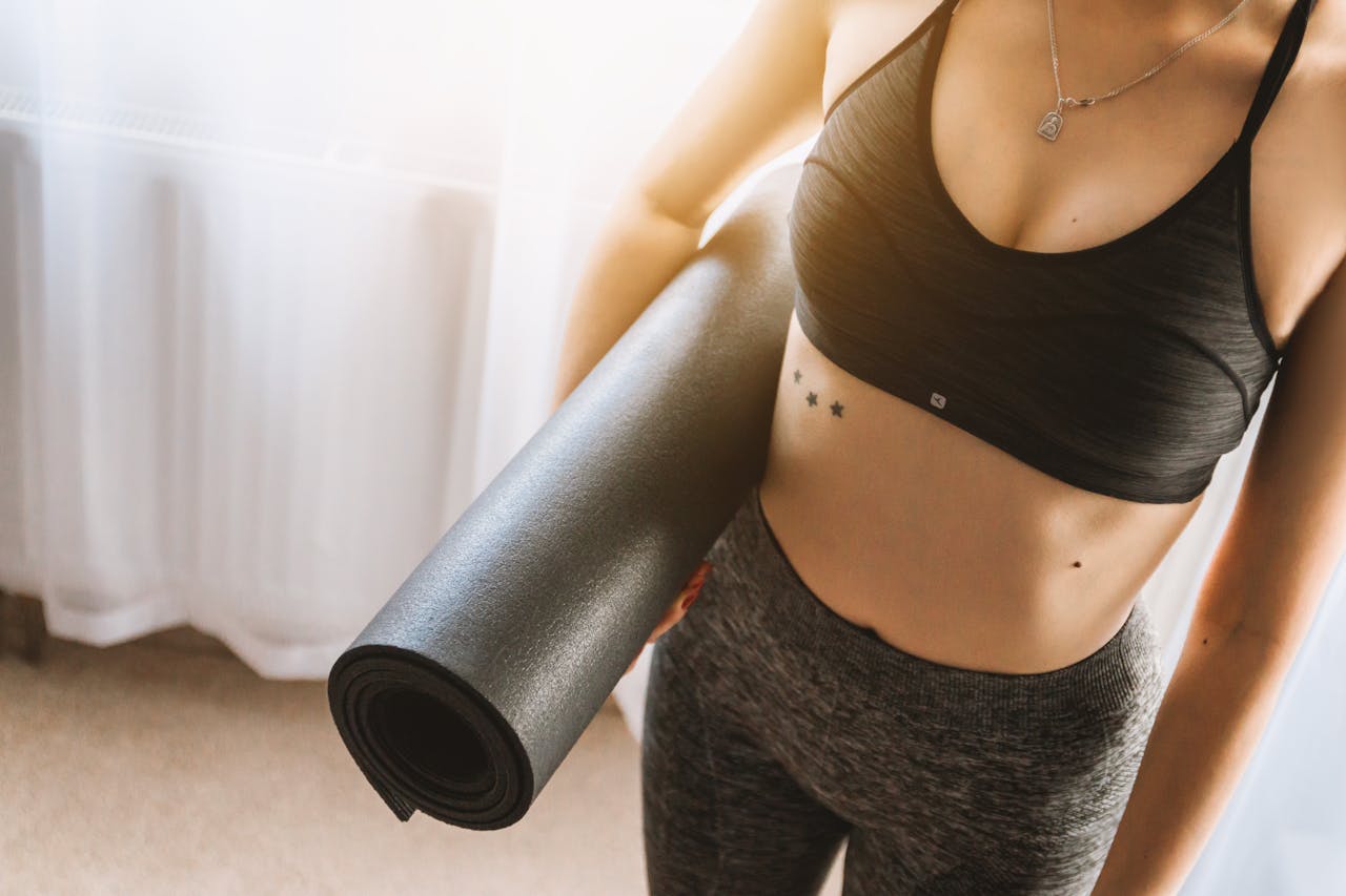 Fit woman in active wear holding yoga mat indoors, ready for workout.