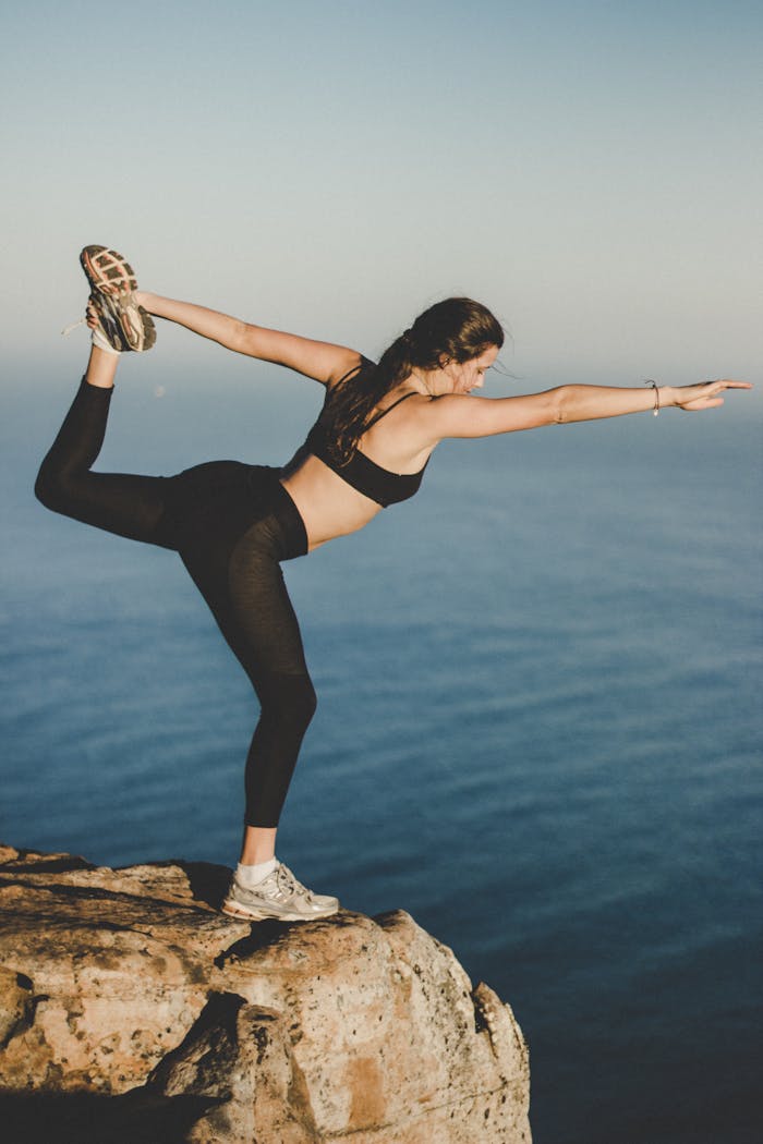 Woman practicing yoga in Dancer's pose on a cliff with ocean view, Cape Town.